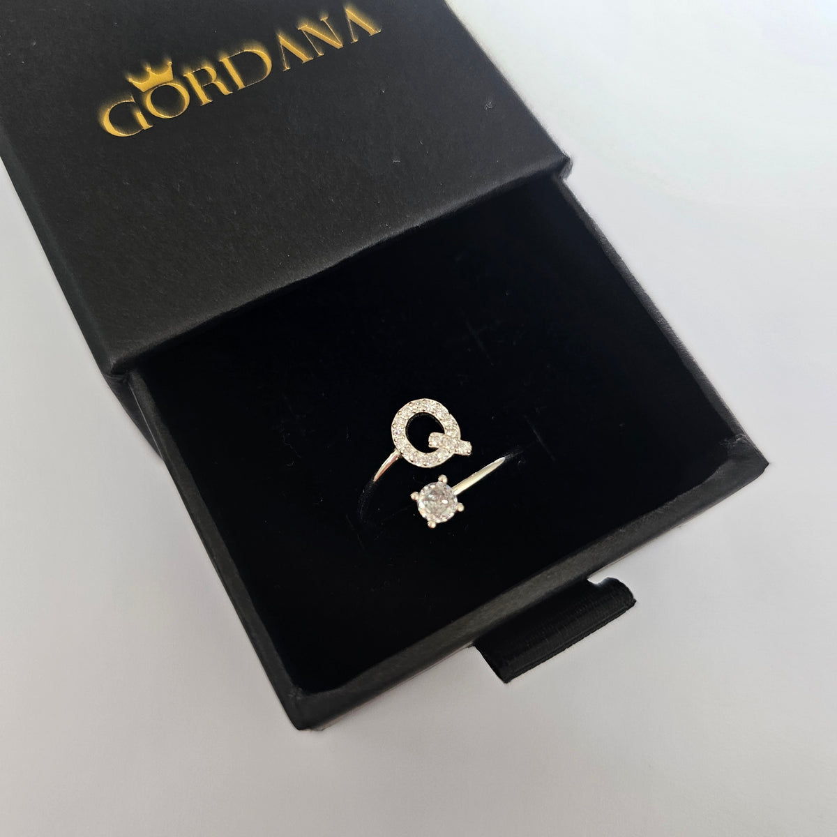 Silver alphabet G and diamond-cut gemstone rings in black jewelry box.