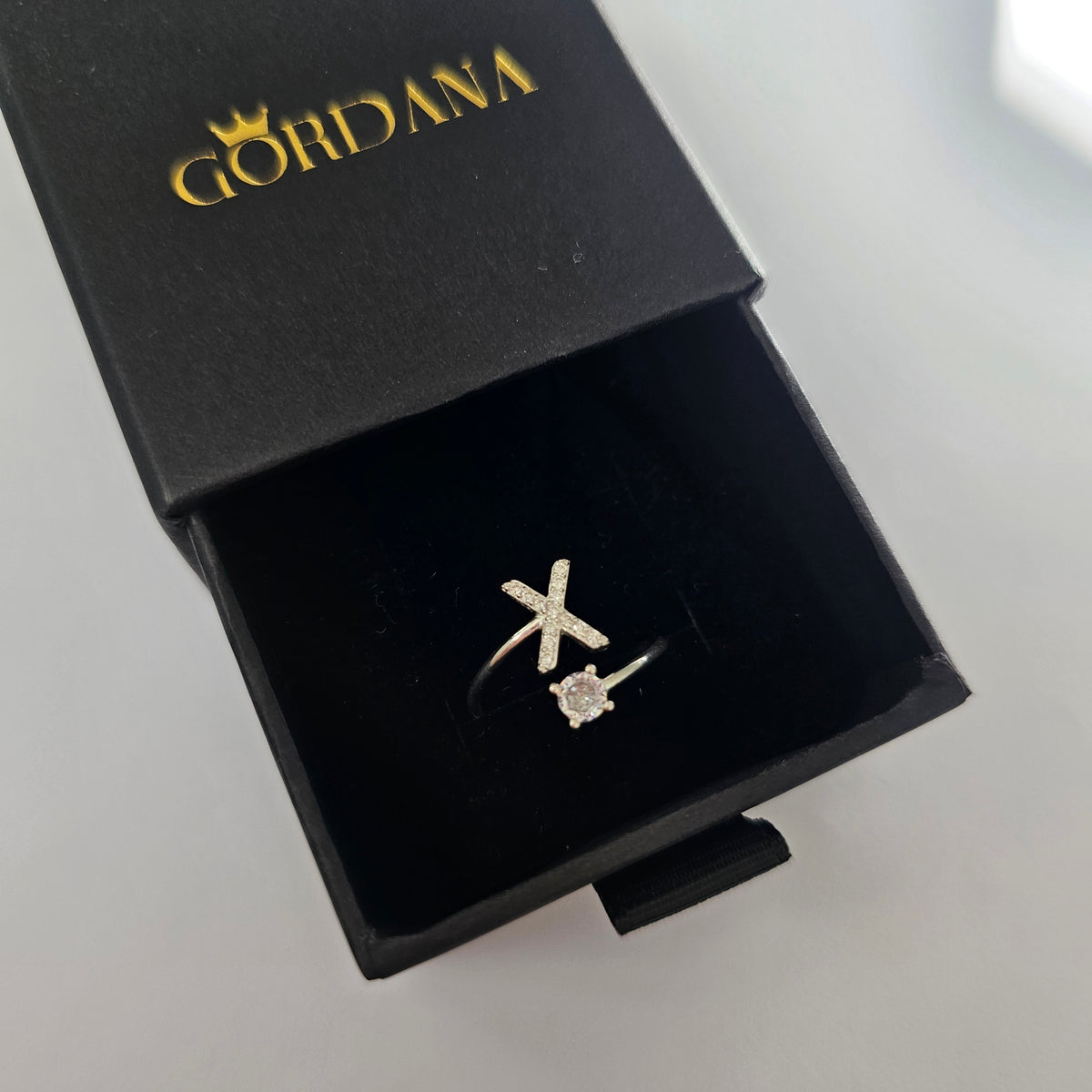 Silver alphabet X ring with small gemstone accent in black velvet box.