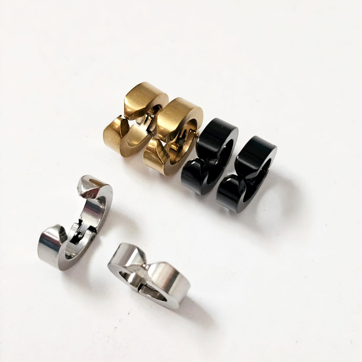 Set of three metallic rings in gold, black, and silver on a white background - Clip-on earrings