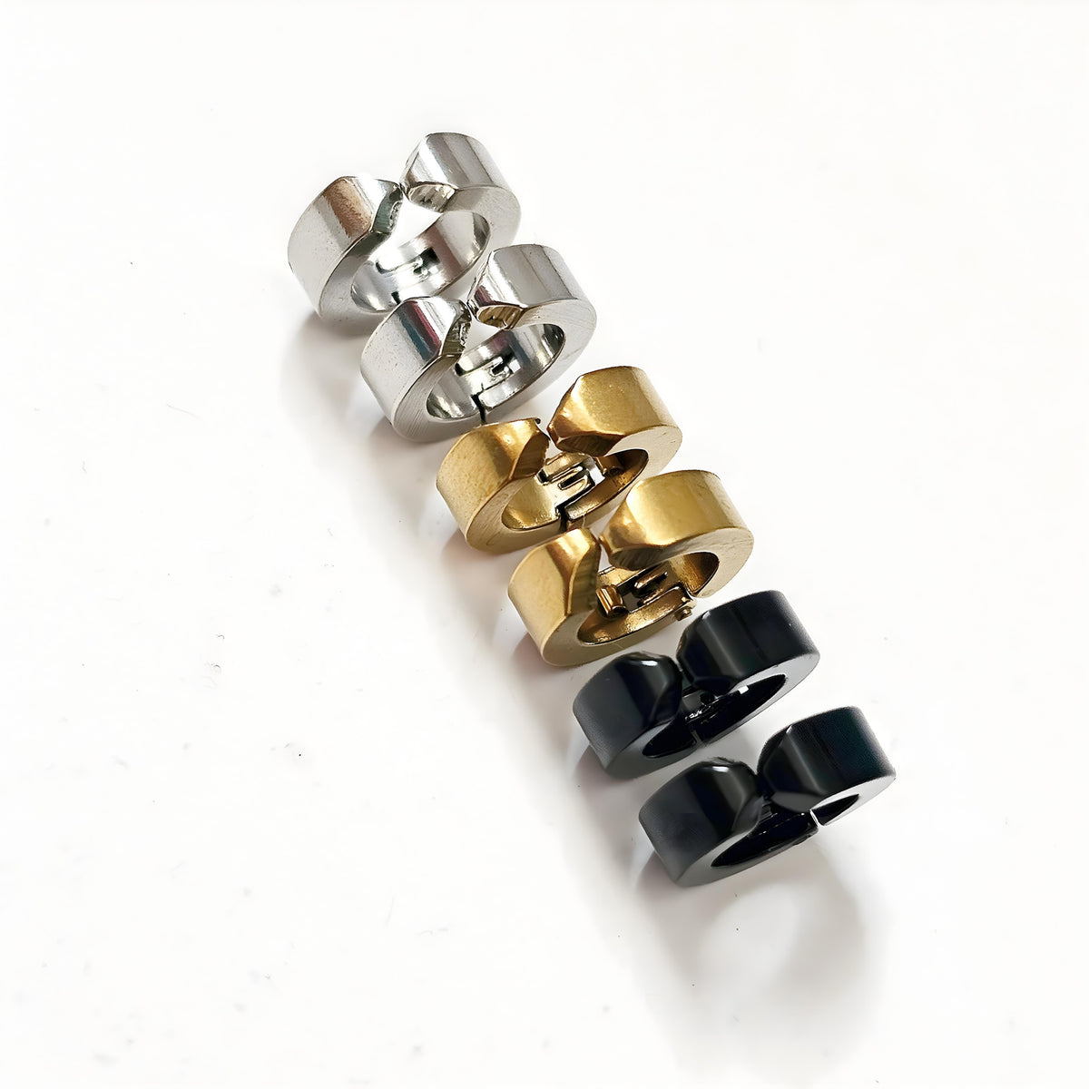 Set of three hoop earrings in silver, gold, and black on a white background