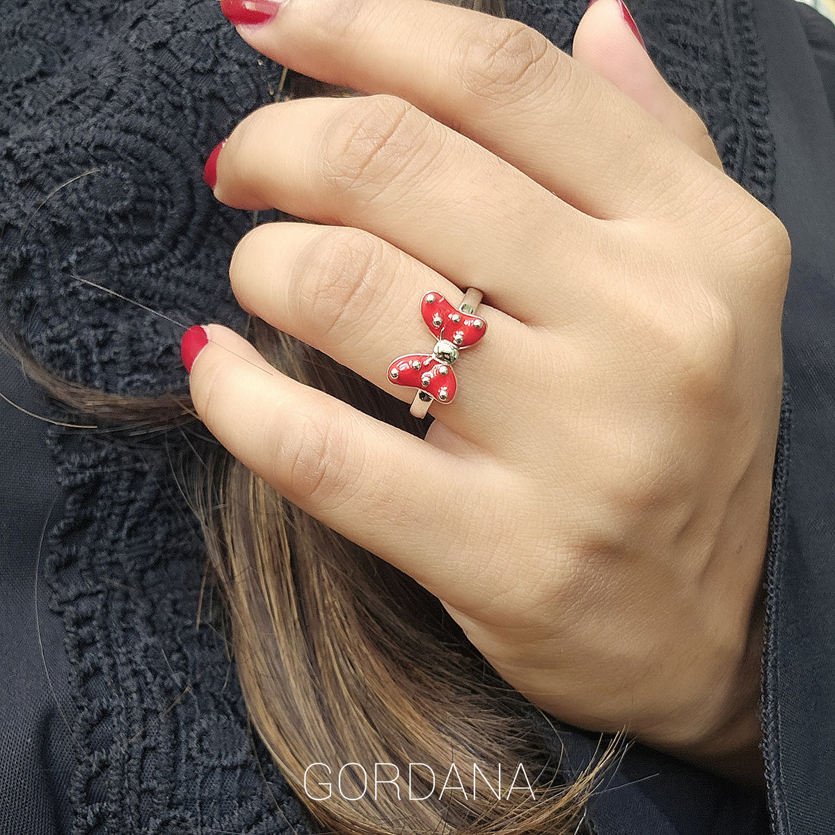 A woman's hand wearing a luxury and cute sterling silver ring with a red and white bow design, held against a background of a black knitted fabric. Gordana jewelry Mauritius.
