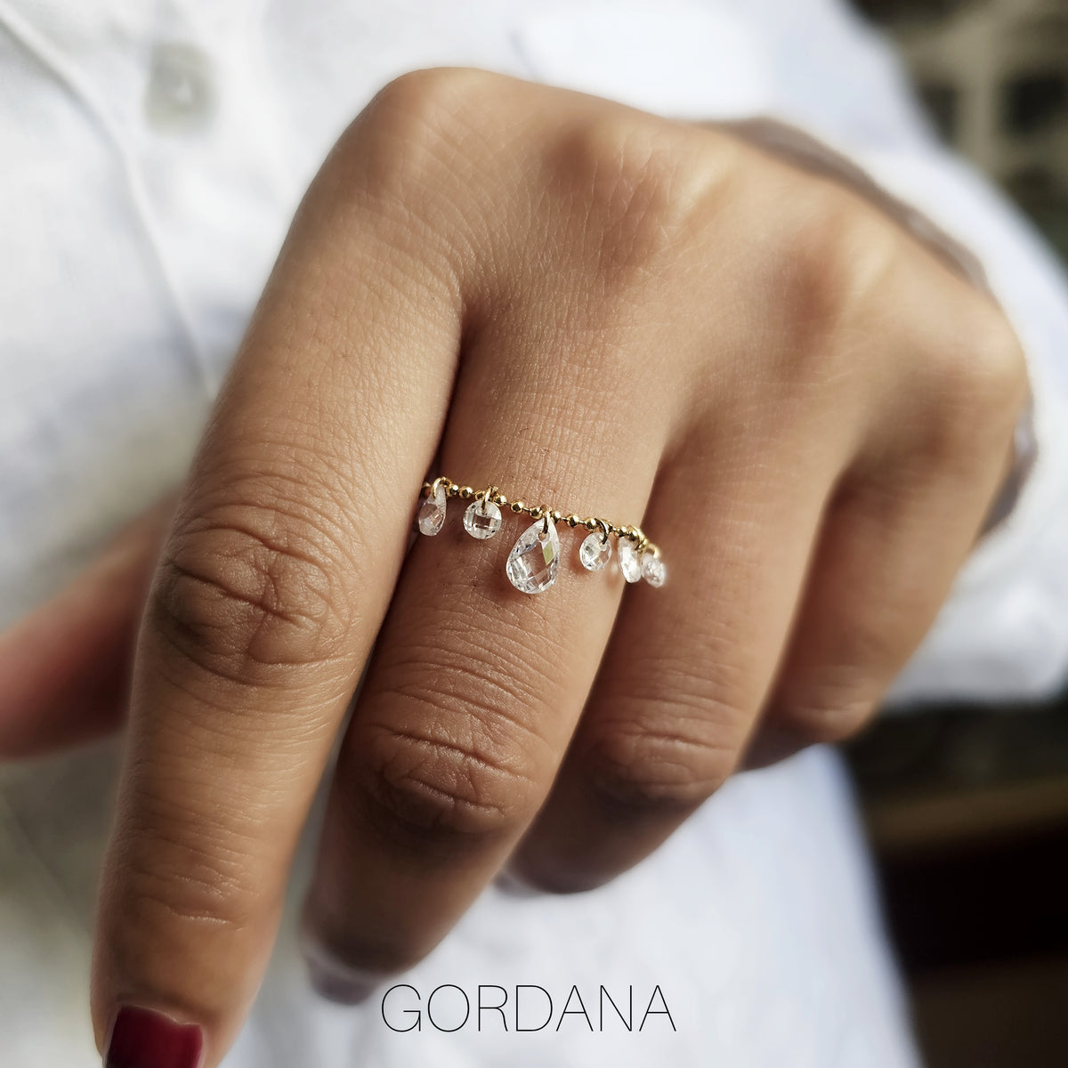 A person's hand wearing a luxury gold stainless steel adjustable chain ring with clear crystal pendants.