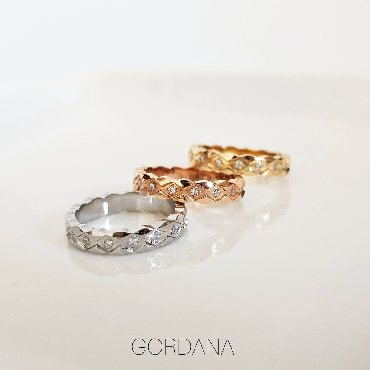 Three stainless steel rings with gold plating and zirconia embellishments, presented on a white surface. Each ring has a different gold plating level, with one appearing silver-colored, one in a rose gold hue, and one in a more traditional gold tone.