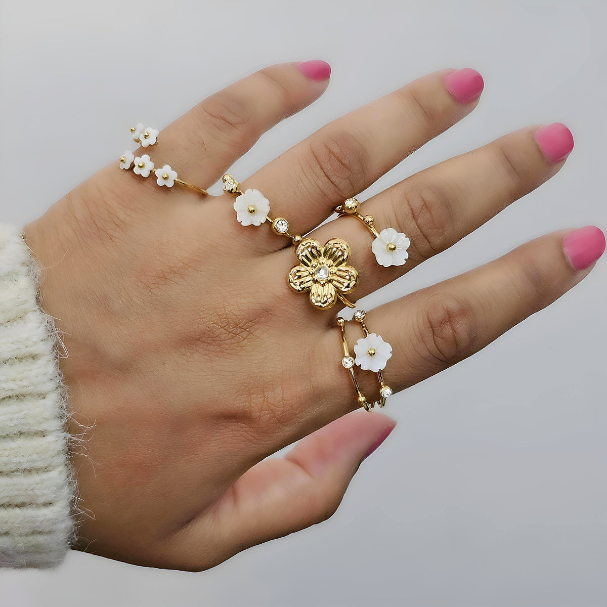Hand wearing gold rings with floral designs on a plain background