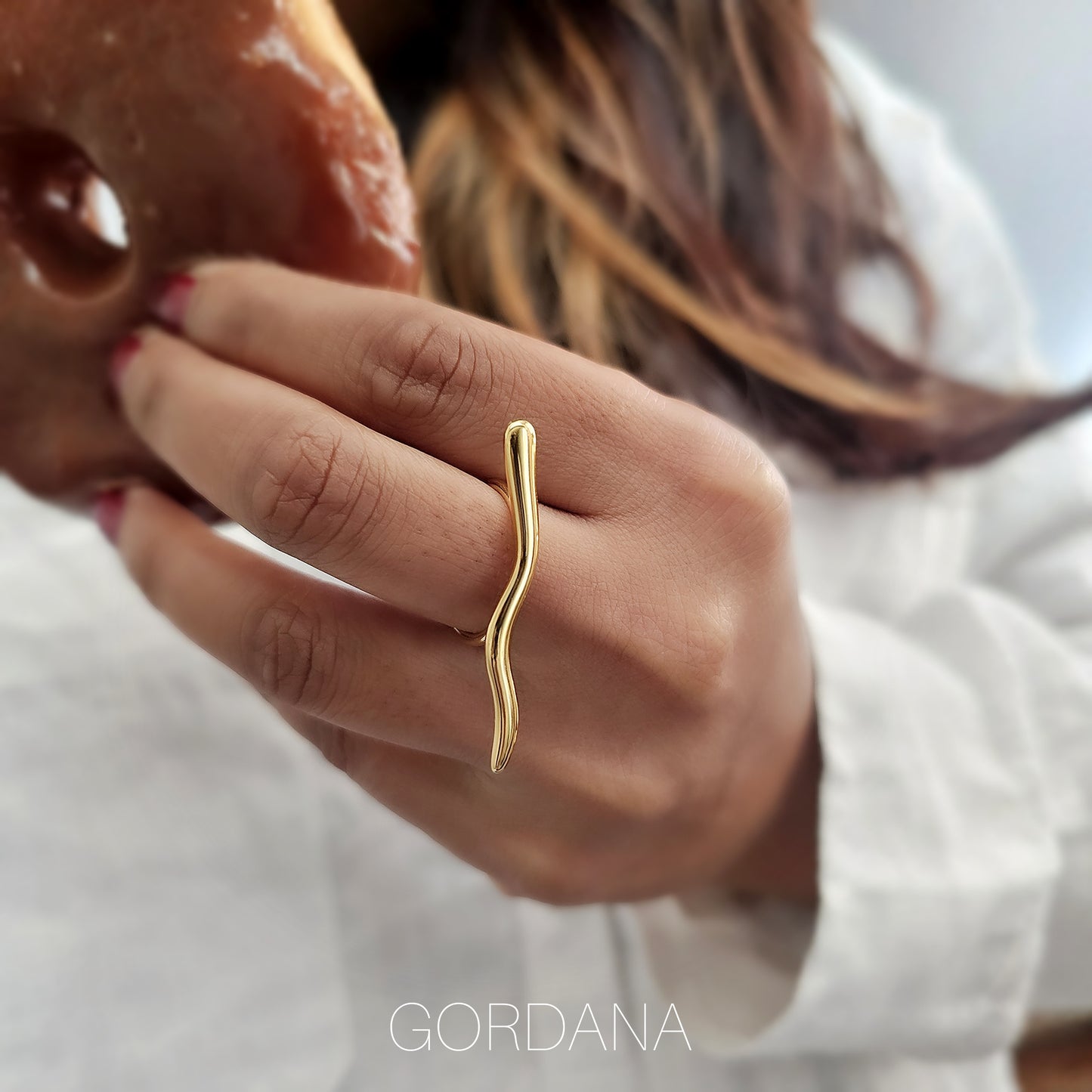Hand wearing a luxury adjustable stainless steel wave ring in gold – Gordana statement ring