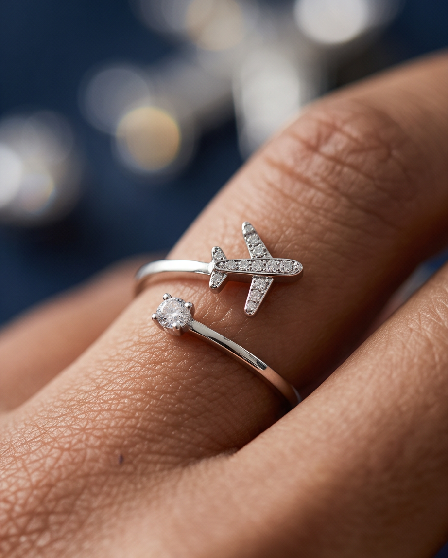 A close-up lifestyle shot of an adjustable sterling silver ring with an airplane design for travel lovers worn on a finger against a dark, blurred background.
