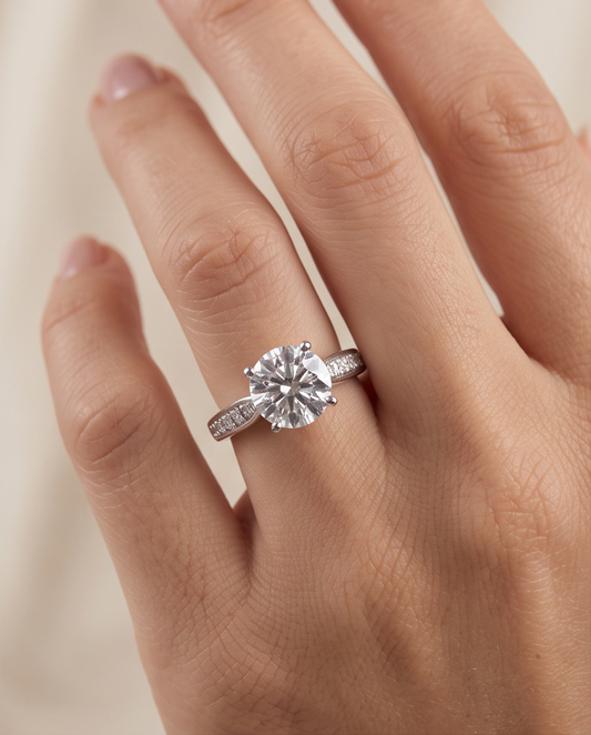 A close-up of a hand wearing a silver engagement ring with a round-cut clear center stone and pavé-setband, a silver solitaire engagement ring for women