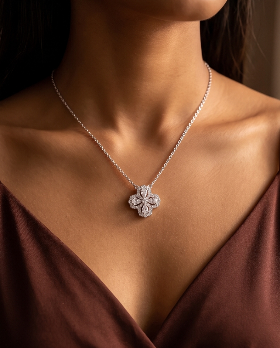 A close-up of a model wearing a delicate silver chain necklace with a four-petal flower pendant paved with small clear stones, styled with a dark brown satin top.