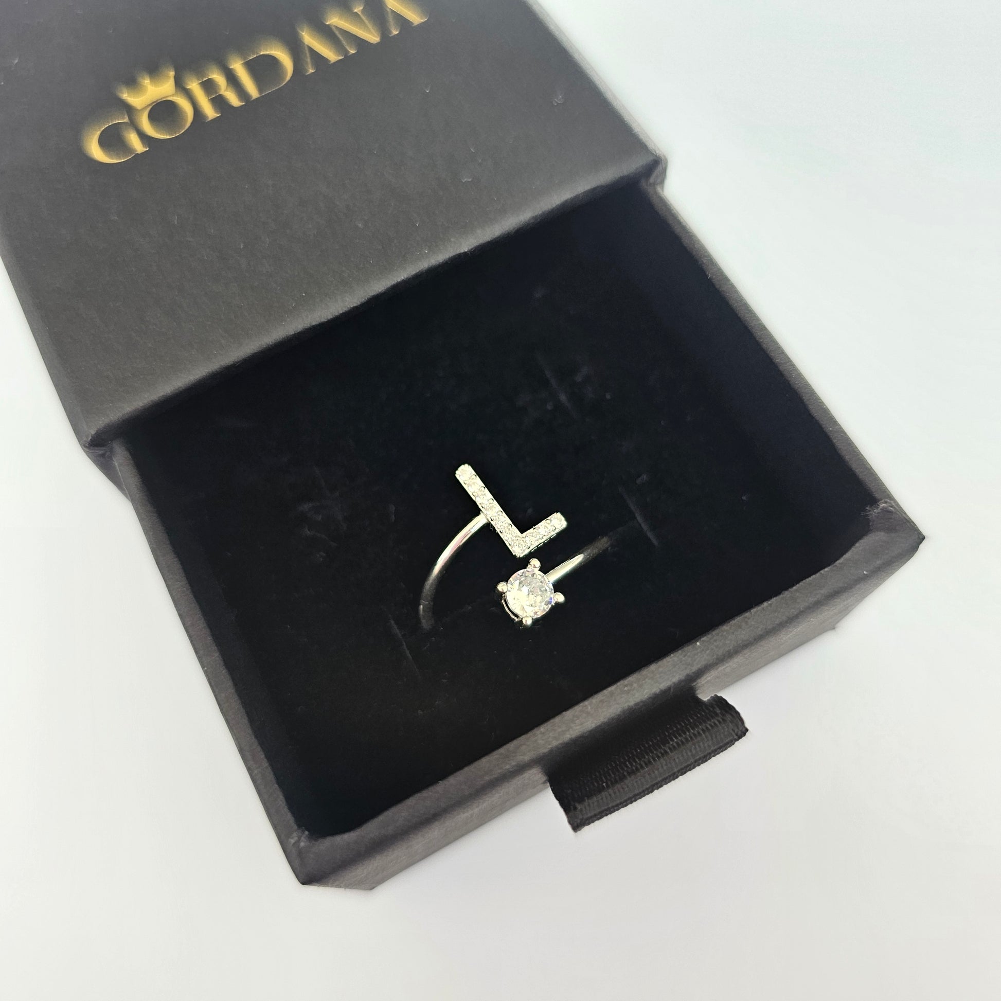 Silver stainless steel alphabet ring with letter L and gemstone detail in black jewelry box, unisex fashion jewelry.