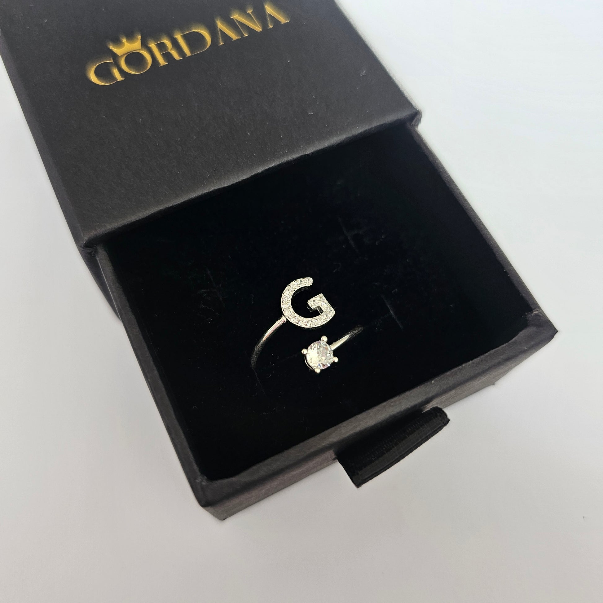 Silver stainless steel unisex fashion ring with letter G and small gemstone in black branded box.
