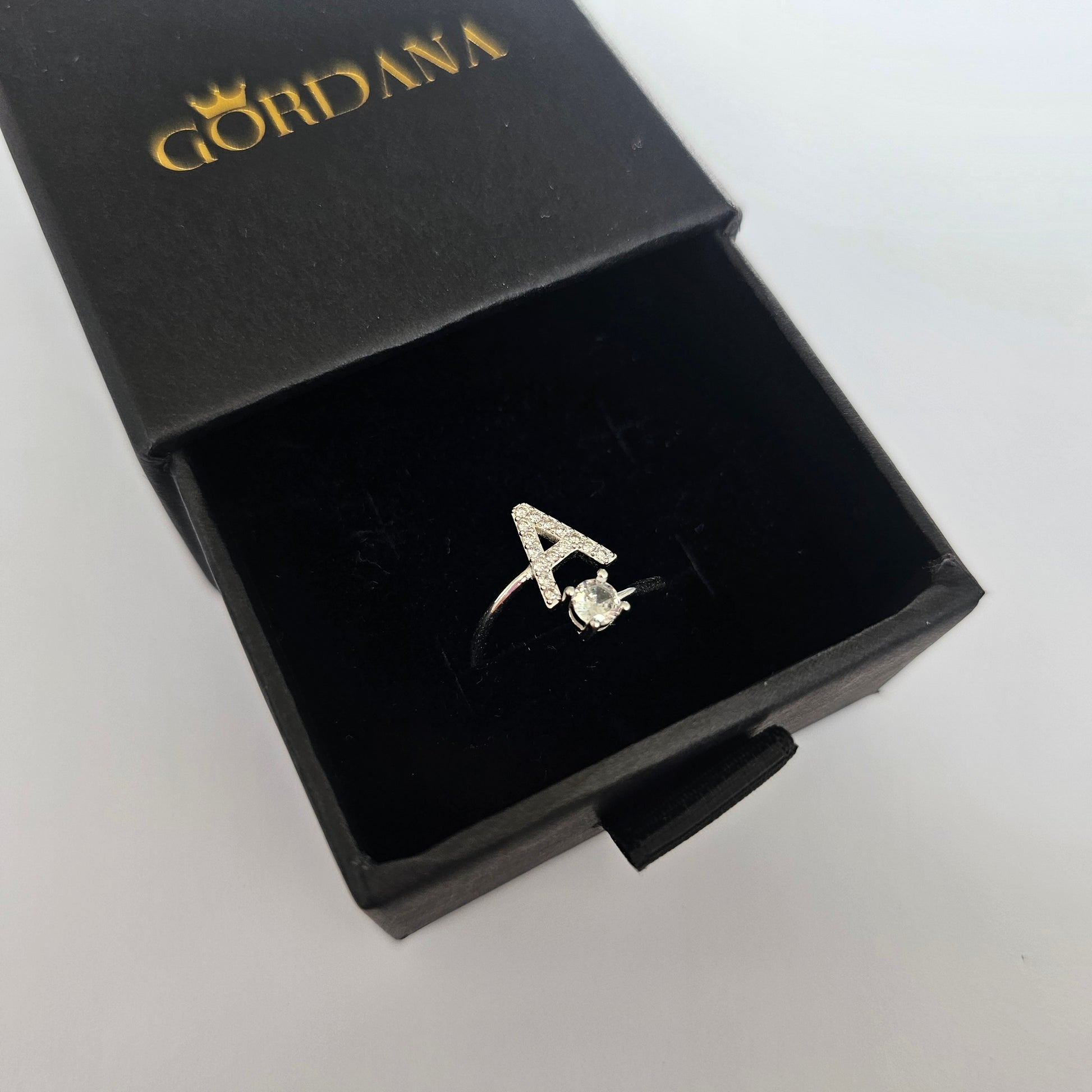 Silver alphabet ring 'A' with a small gemstone, elegant stainless steel jewelry in a black box, unisex fashion jewelry.