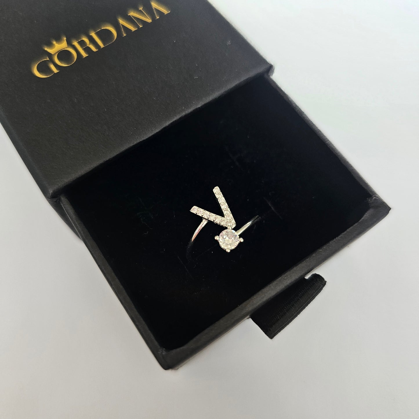 Silver stainless steel V-shaped alphabet ring with a sparkling gemstone, stylish unisex fashion jewelry in luxury black box.