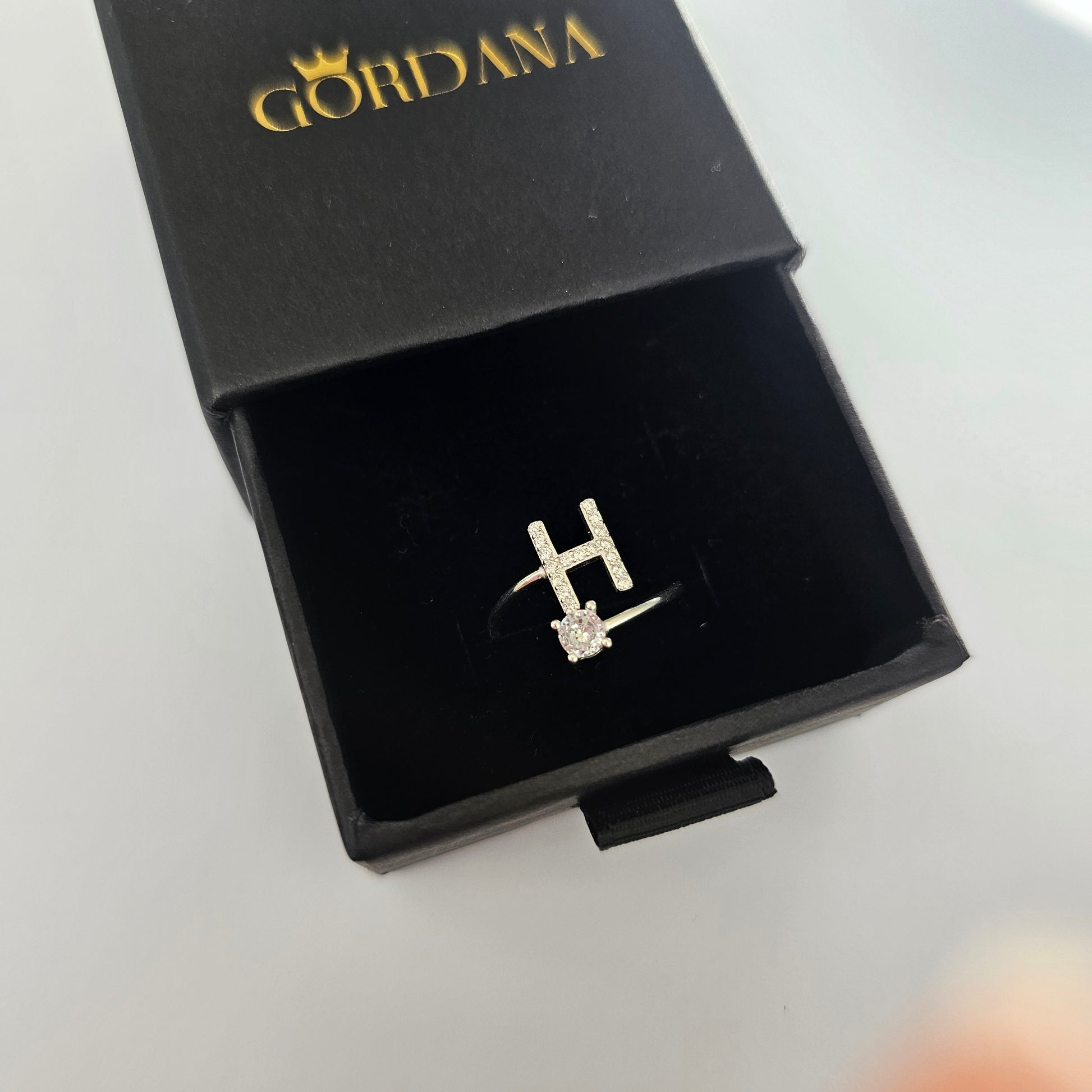 Silver stainless steel alphabet ring with H initial and small gemstone in black jewelry box, unisex fashion jewelry.