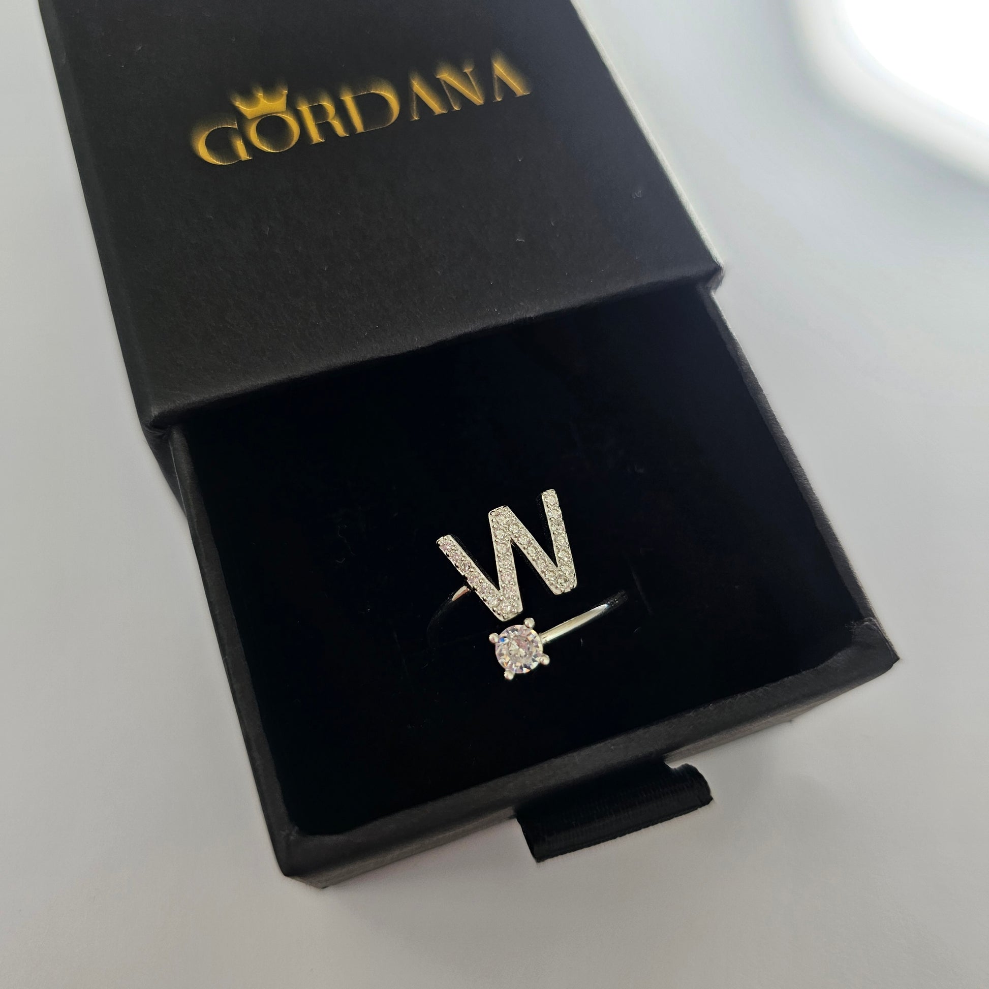 Elegant silver letter W ring with a sparkling gemstone, stainless steel jewelry in a black branded box, unisex fashion.