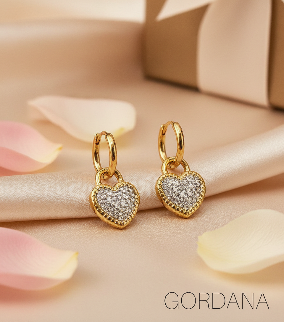 Gold heart-shaped earrings with clear stones on a beige surface with pink petals, featuring the brand 'Gordana'.- Heart Lock stainless steel Earrings