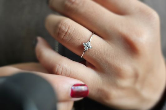 A hand wearing a luxury minimalist silver ring with four petals flower design. 