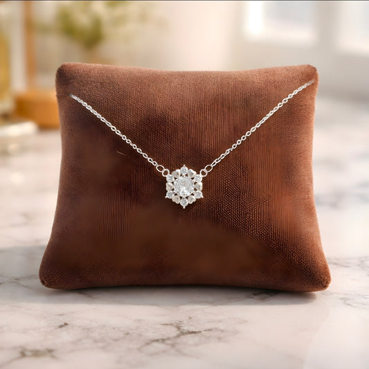 Silver necklace with a floral pendant on a brown pillow against a marble background