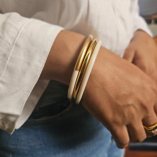 A close up of a woman wearing a stack of three elegant resin and gold plated stainless steel bangles.