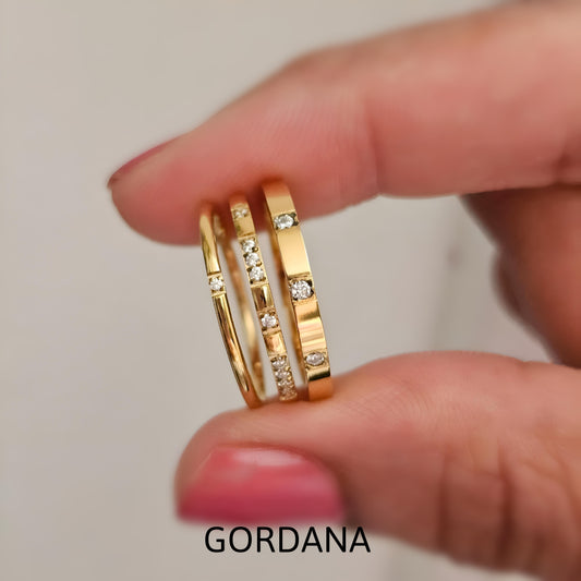 Gold rings with diamonds on a finger, featuring the brand 'Gordana'. Trio Rings - Stainless steel