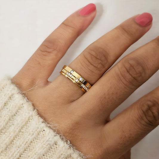 Gold ring with small diamonds on a hand with pink nail polish against a neutral background