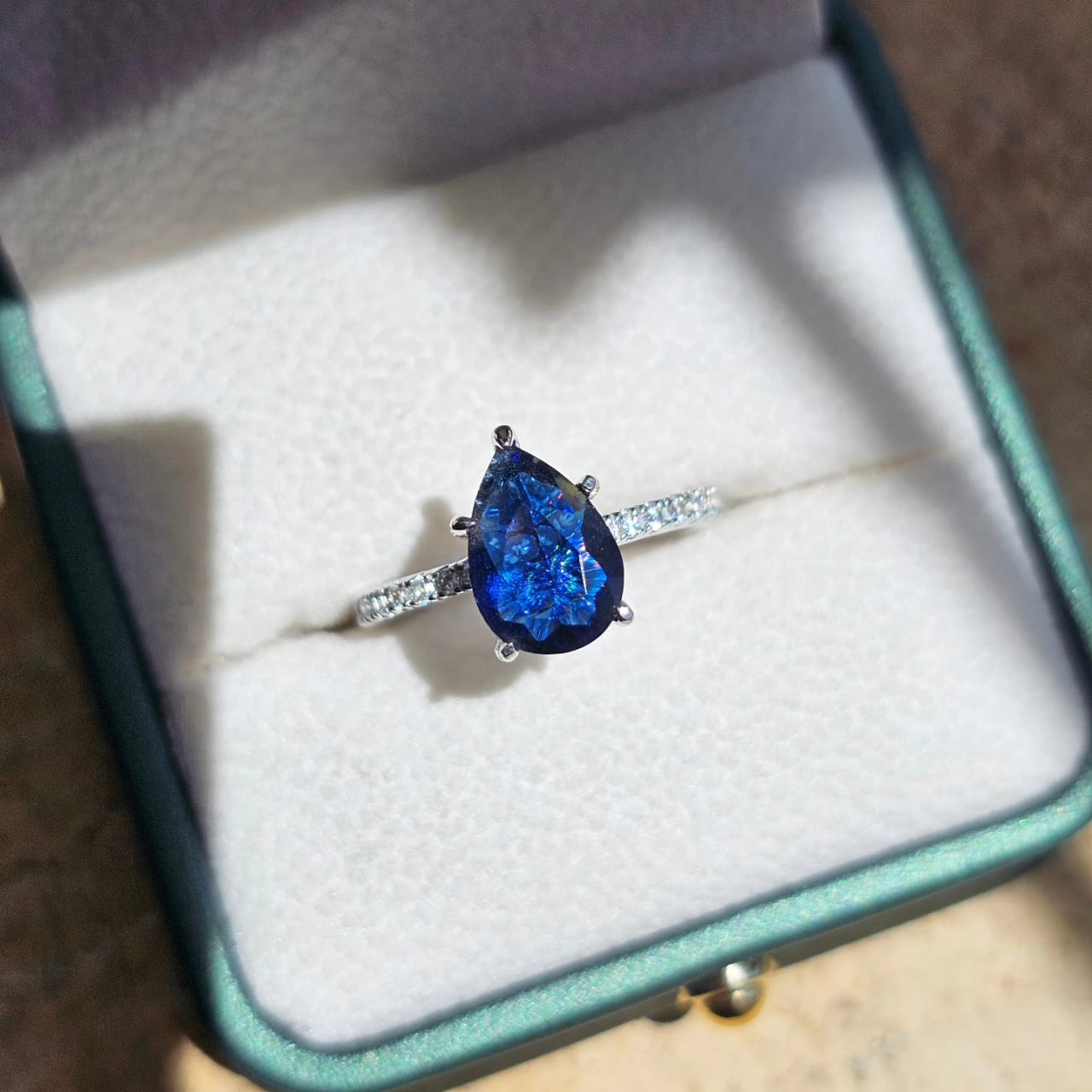 Silver jewelry ring featuring a pear-shaped blue gemstone on a stainless steel band with small clear stones, unisex fashion.