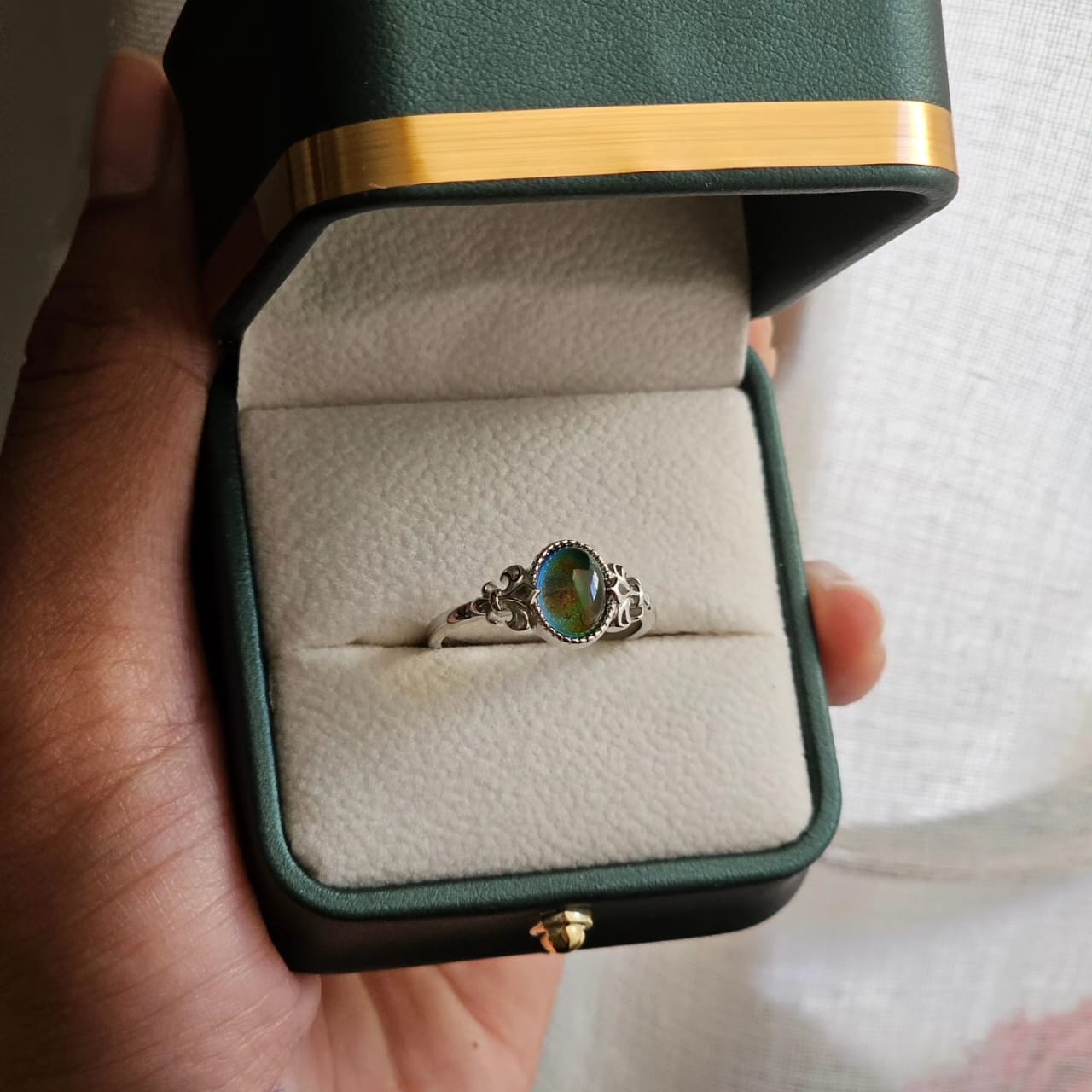 Silver tone mood ring with a round iridescent gemstone and intricate filigree band in a green velvet box.