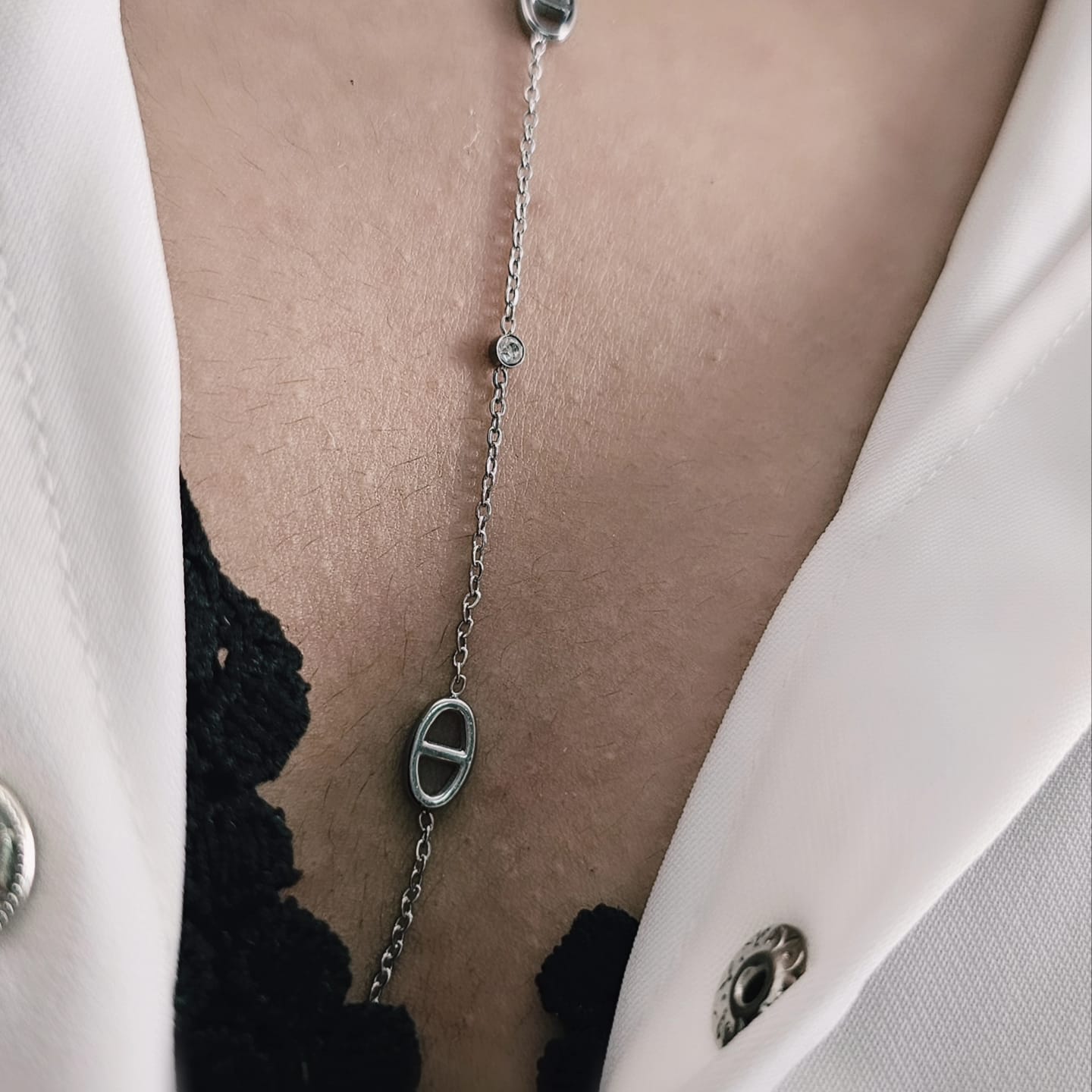 Silver stainless steel necklace with oval pendant and adjustable chain on black lace and white blazer background.