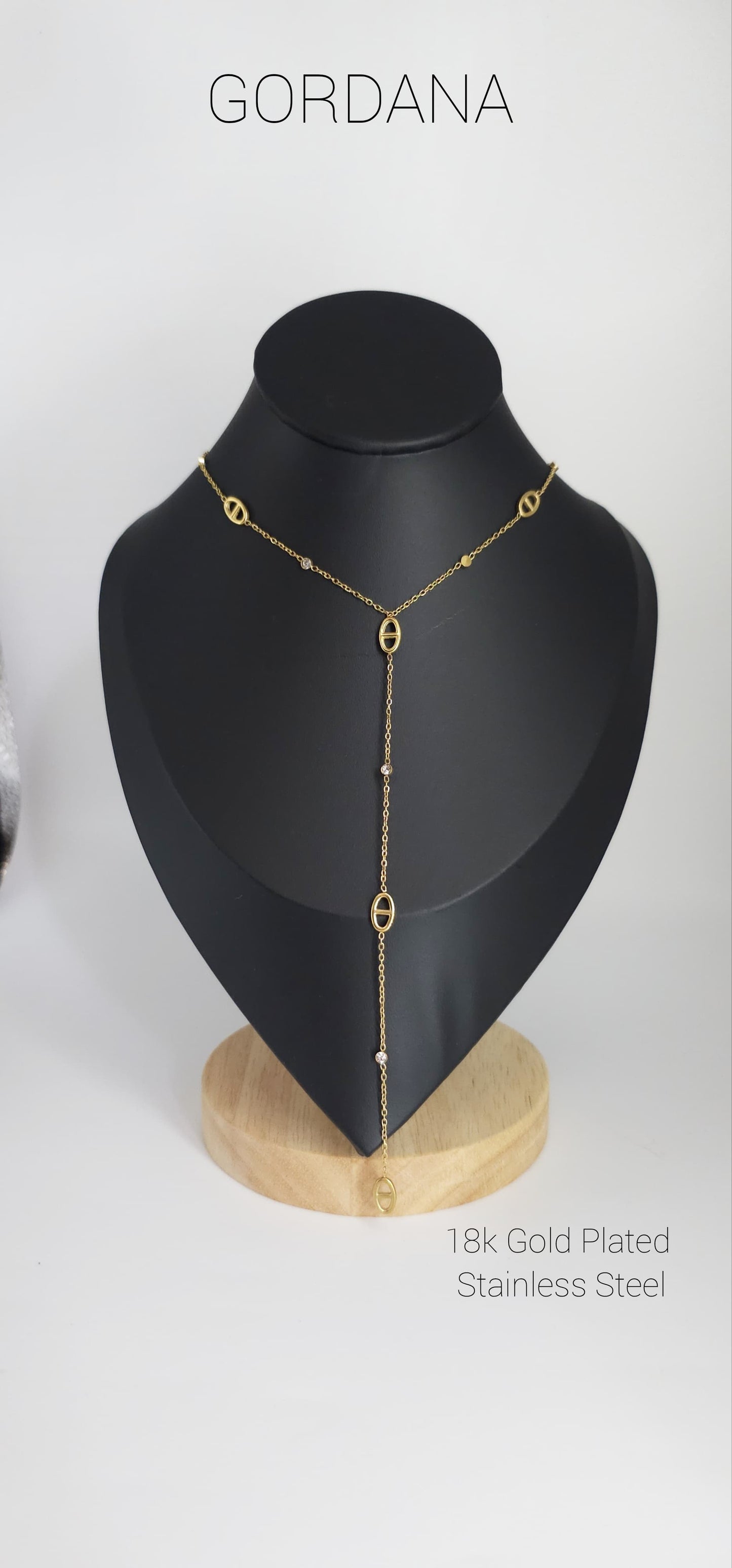 Gold-plated stainless steel necklace with minimalist chain and vertical drop pendant on black display bust.