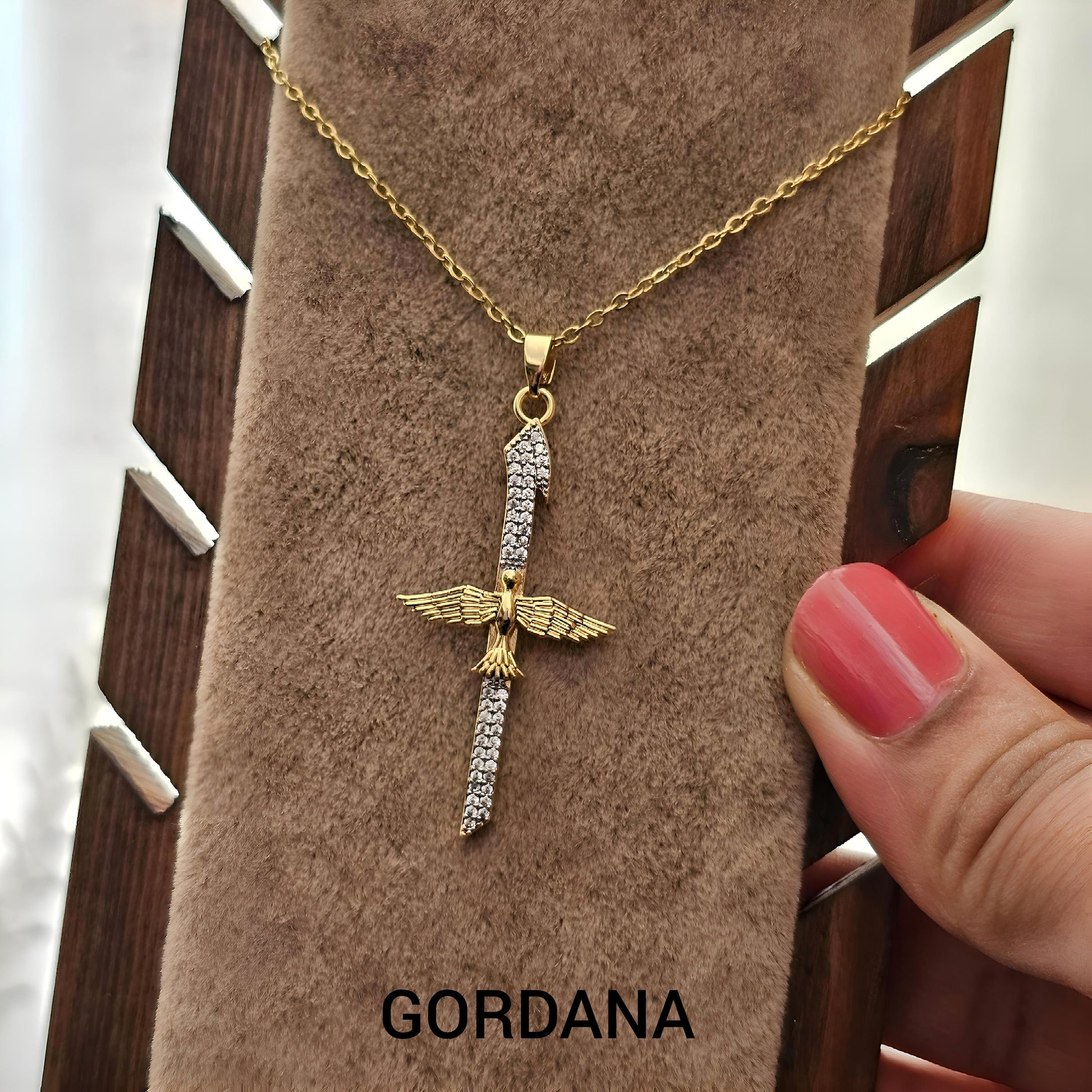 Gold necklace with an eagle pendant on a brown velvet stand with 'Gordana' branding - Winged_Blade_Pendant_-_Gordana_Jewelry