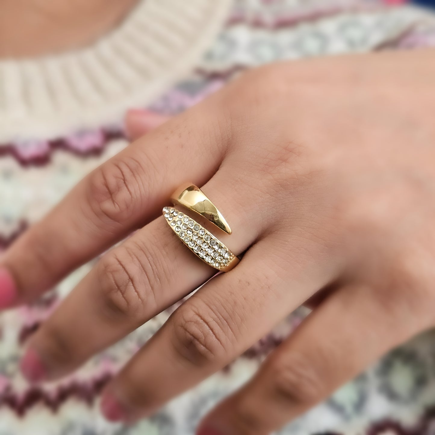 Gold ring with diamond accents on a person's finger against a patterned background