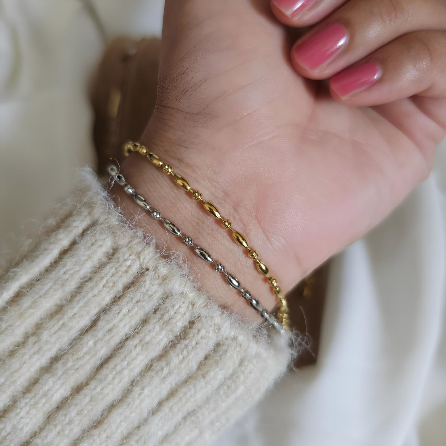 Close-up of a hand wearing two gold bracelets on a neutral background