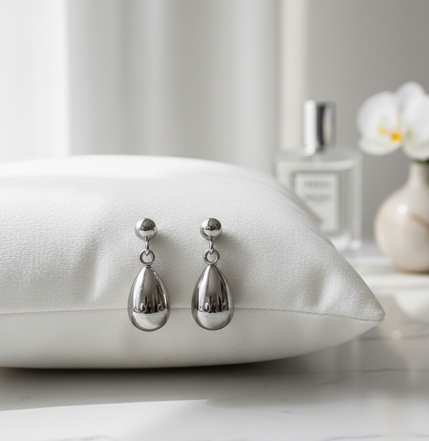 Silver teardrop earrings on a white pillow with a blurred background