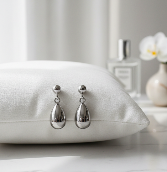 Silver teardrop earrings on a white pillow with a blurred background