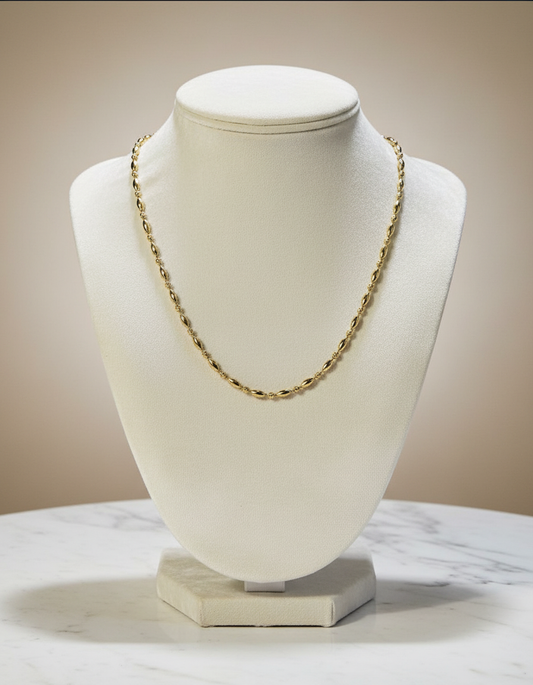 Gold chain necklace on a white bust against a beige background