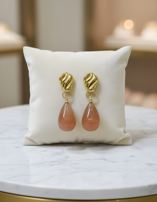 Gold earrings with pink stones pendant on a white cushion