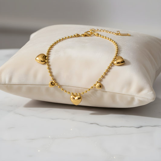 Gold bracelet with heart-shaped charms on a white pillow