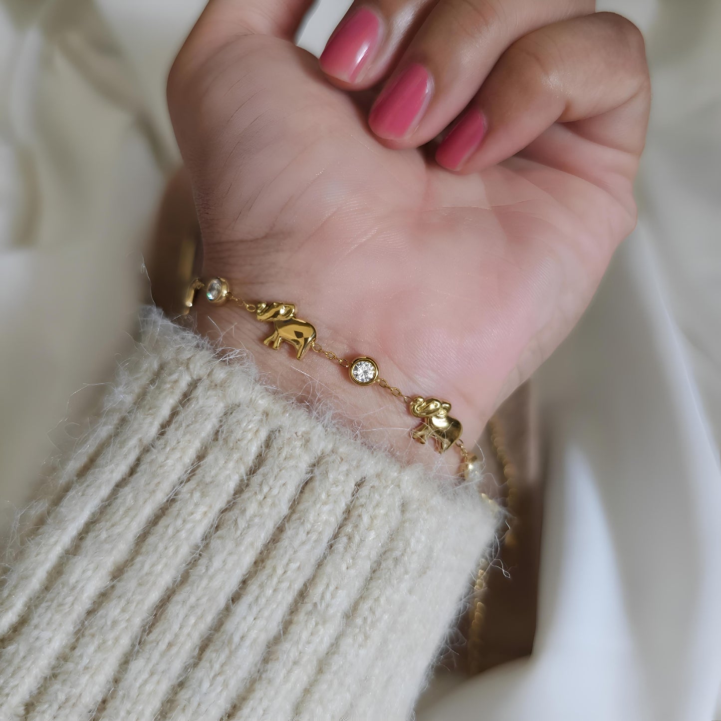 Gold bracelet with elephant charms on a wrist against a neutral background
