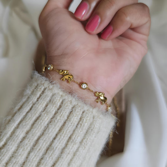 Gold bracelet with elephant charms on a wrist against a neutral background