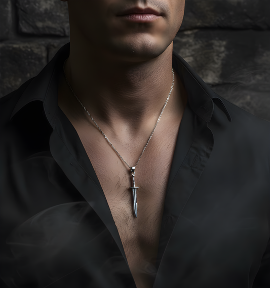 Man wearing a black shirt with a silver necklace featuring a dagger pendant against a dark stone wall.