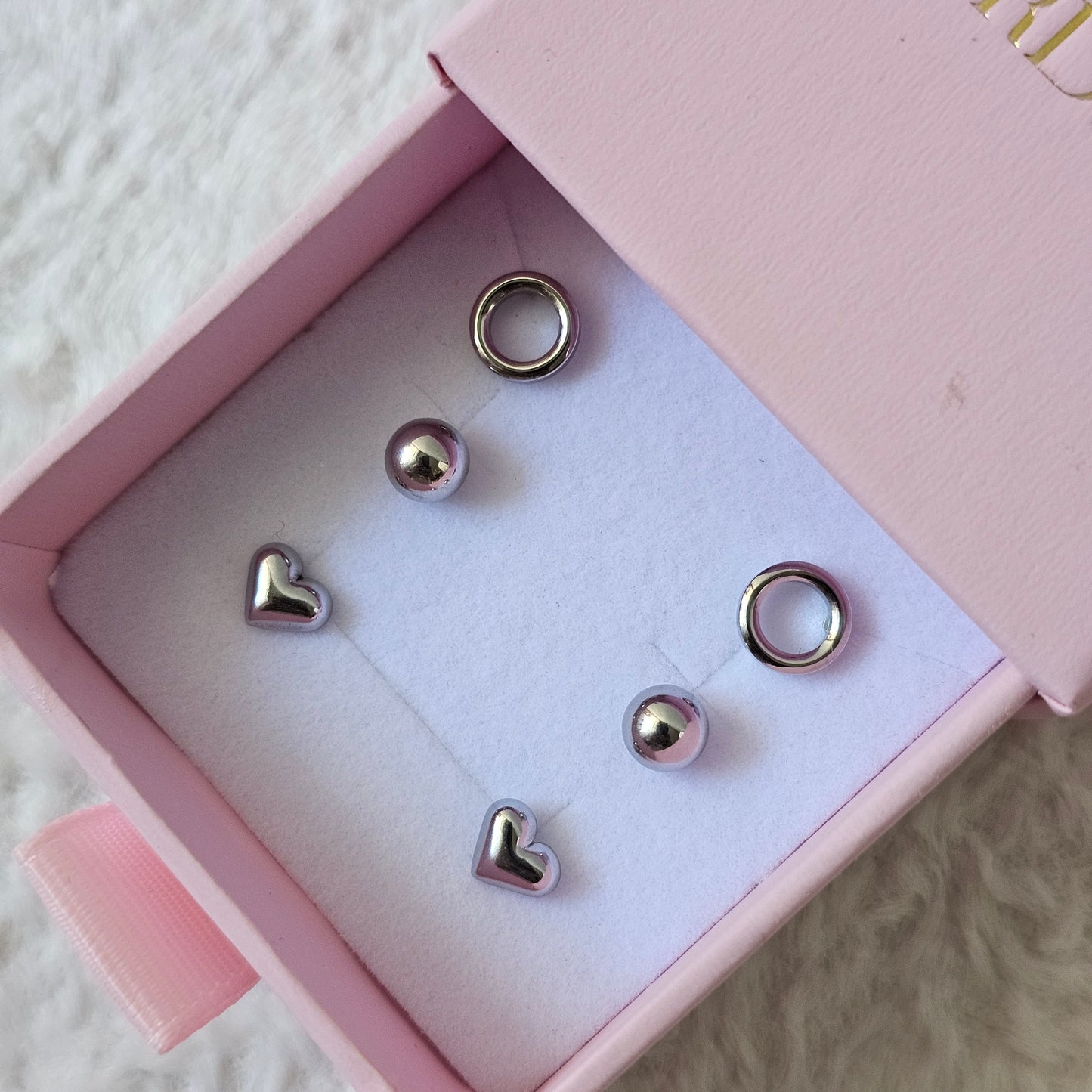Trio set of stainless steel and silver jewelry earrings with polished ball, heart, and hoop designs in a pink box, unisex.