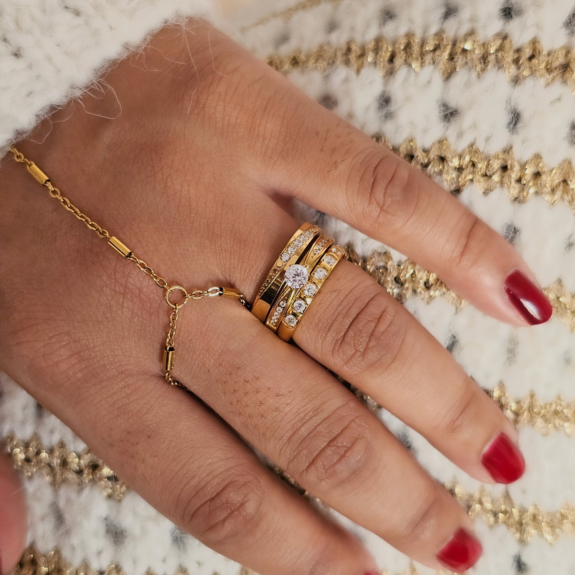 Hand wearing gold jewelry with a textured gold background. hand wearing gold stack rings and a minimalist handchain.