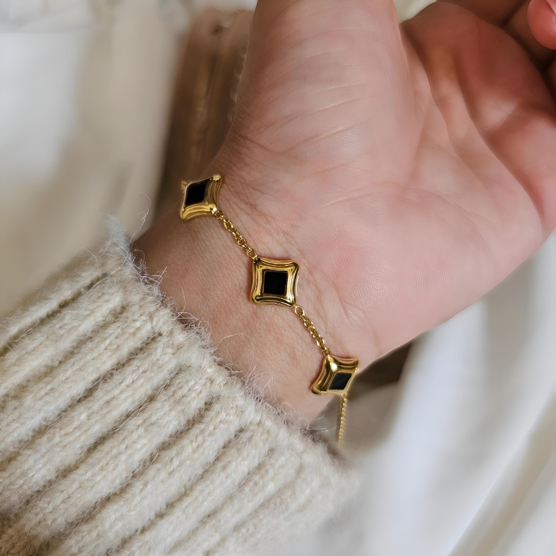 Gold bracelet with black stones on a wrist against a neutral background