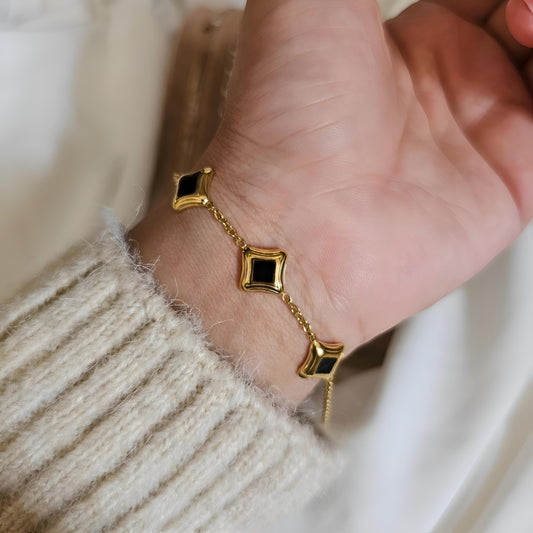 Gold bracelet with black stones on a wrist against a neutral background
