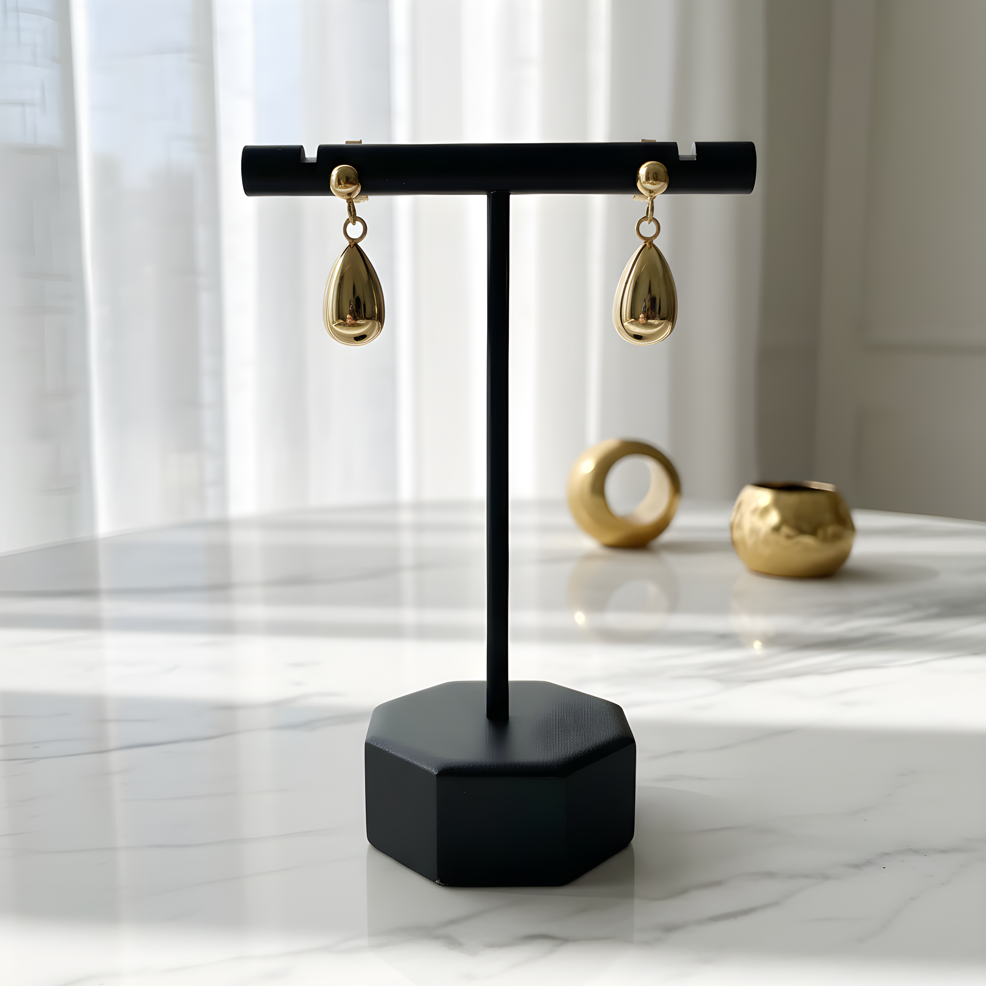 Black jewelry stand with gold teardrop earrings on a marble surface