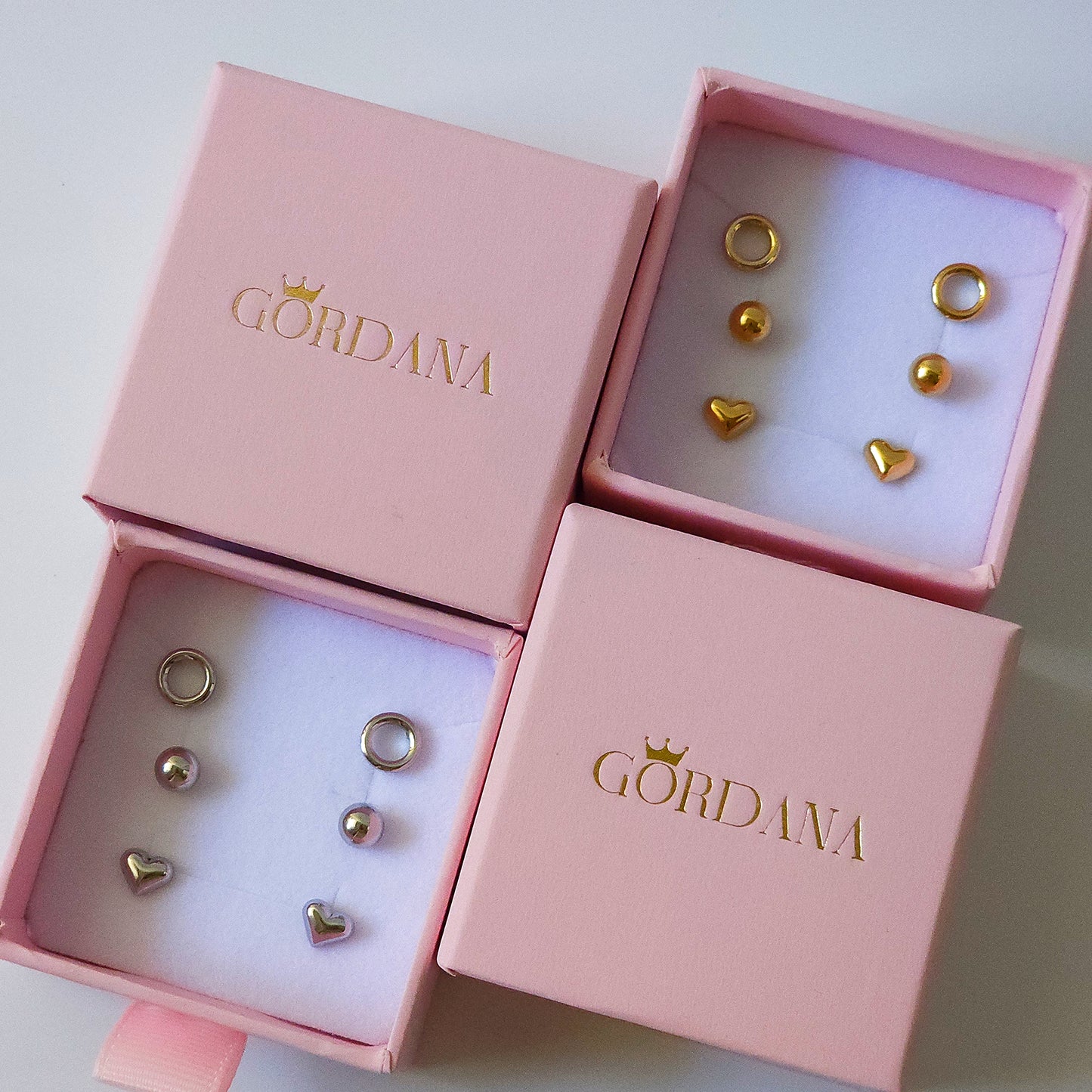 Trio set of gold and silver stainless steel fashion earrings with gemstone accents in pink Gordana boxes.