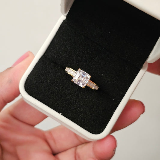 Gold princess-cut diamond ring in a black jewelry box held by a hand