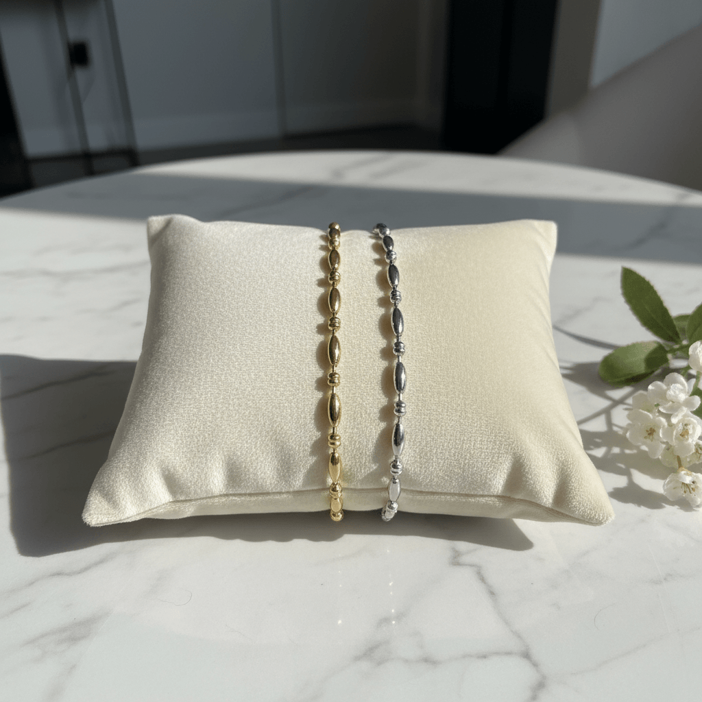 Two bracelets on a textured pillow with a marble surface and plant in the background