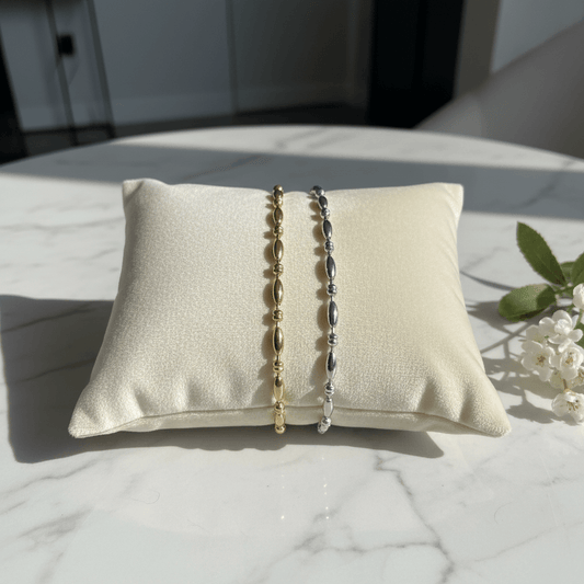 Two bracelets on a textured pillow with a marble surface and plant in the background