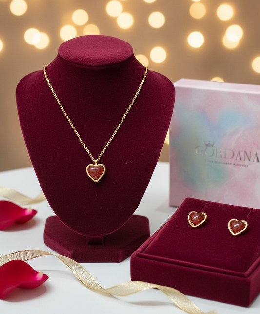 Gold Jewelry set with heart-shaped agate pendant and earrings on a red velvet stand with blurred lights in the background.