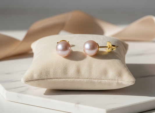 Pair of pink pearl earrings on a beige cushion with a neutral background